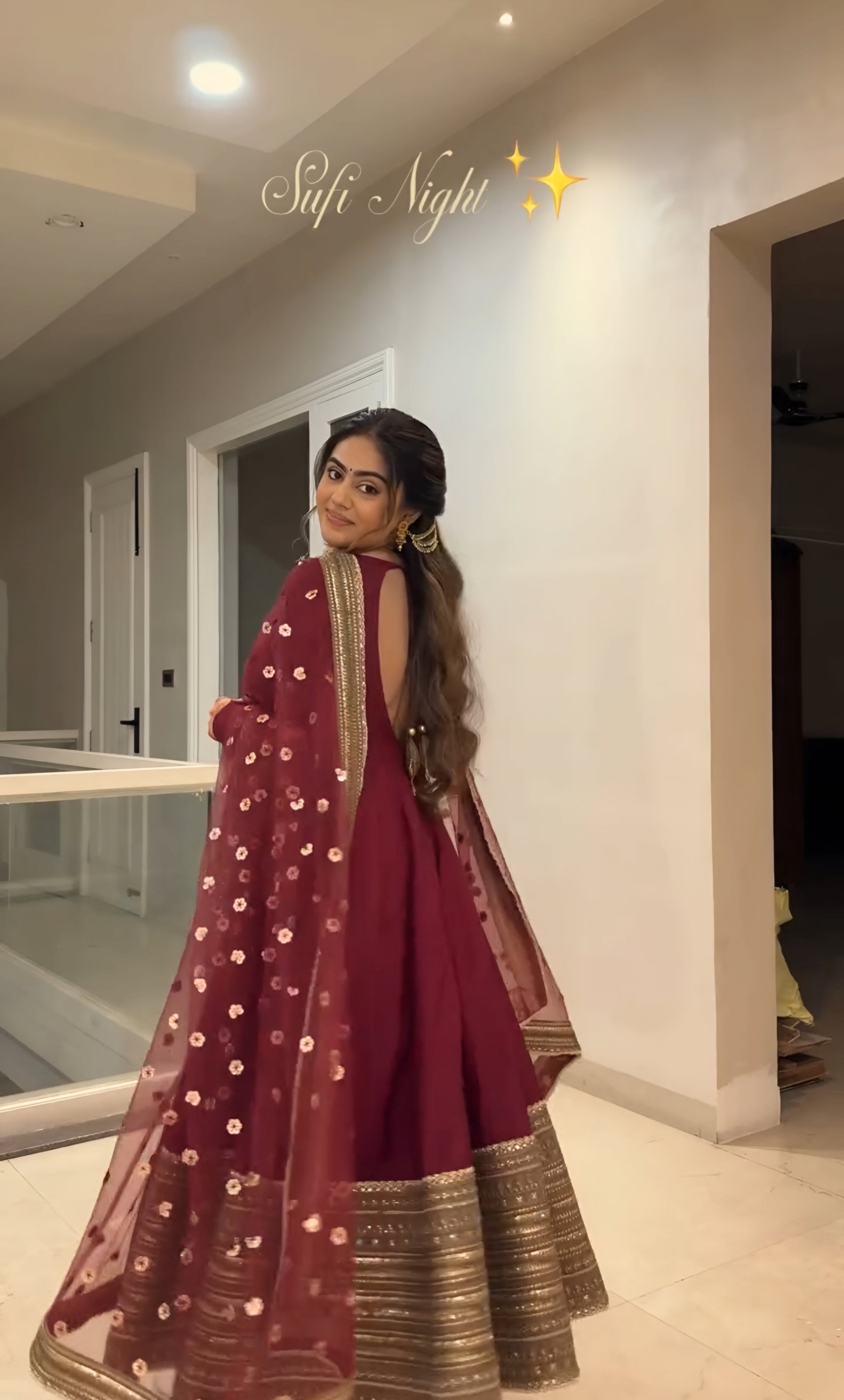 Woman in a maroon traditional outfit with gold details standing indoors.