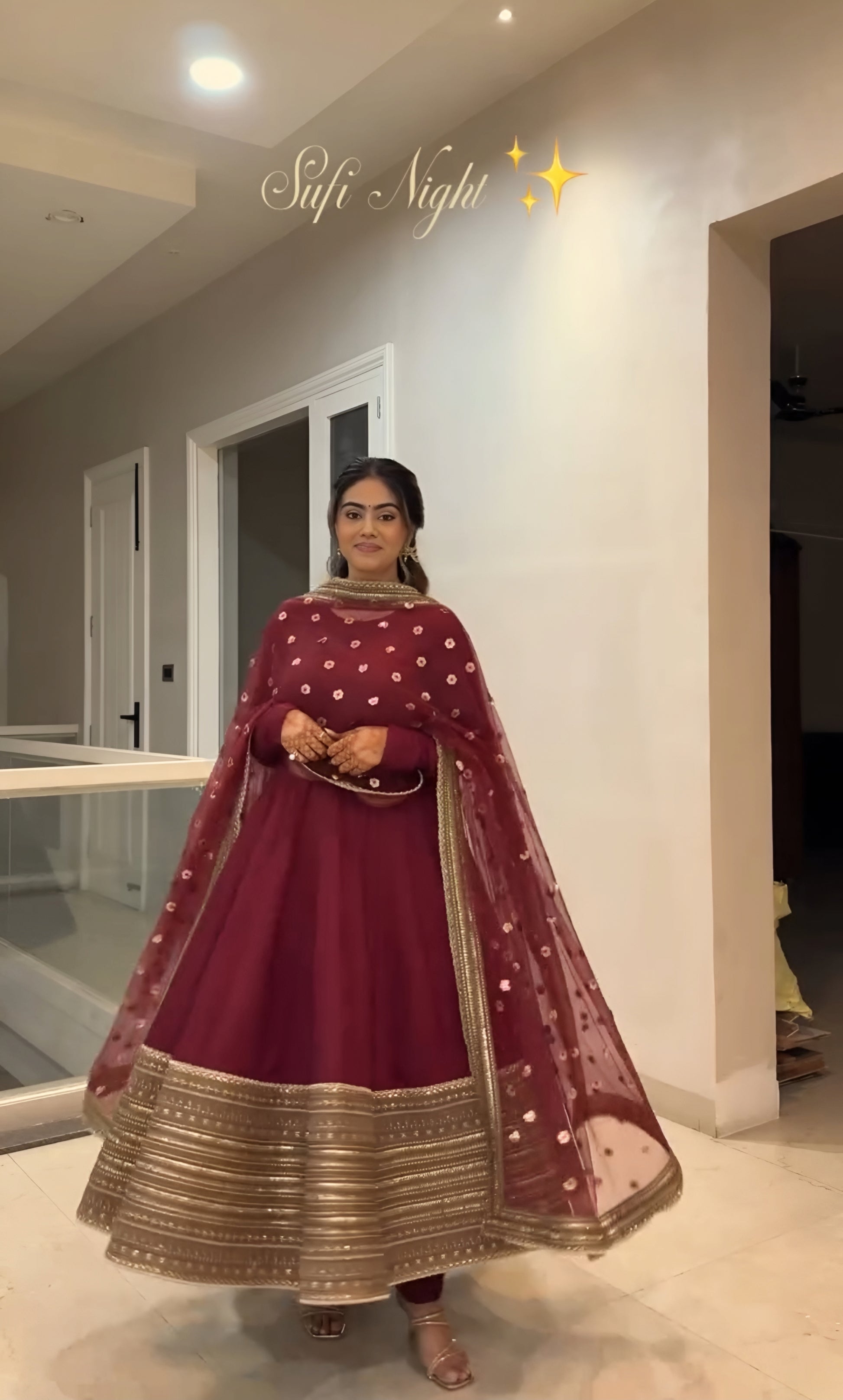 Woman in a maroon traditional outfit with gold details indoors.
