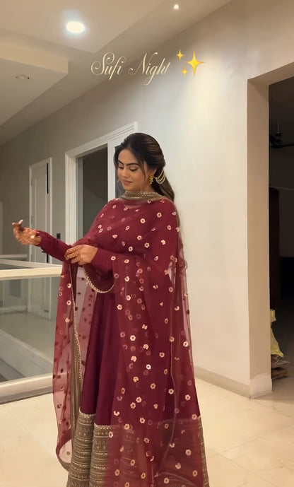 Woman in a maroon saree with gold patterns standing indoors.