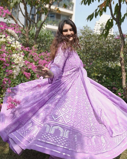 Woman in a purple dress with floral patterns standing in a garden.