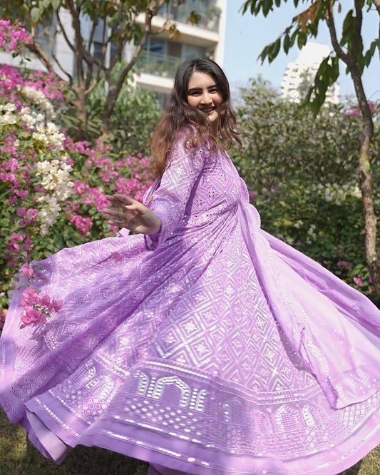 Woman in a purple dress with floral patterns standing in a garden.