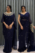 Woman wearing a navy blue saree with intricate designs against a gray curtain background