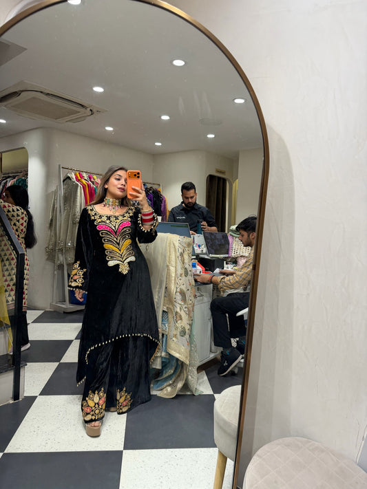 Woman taking a mirror selfie in a store, wearing a black outfit with colorful patterns.